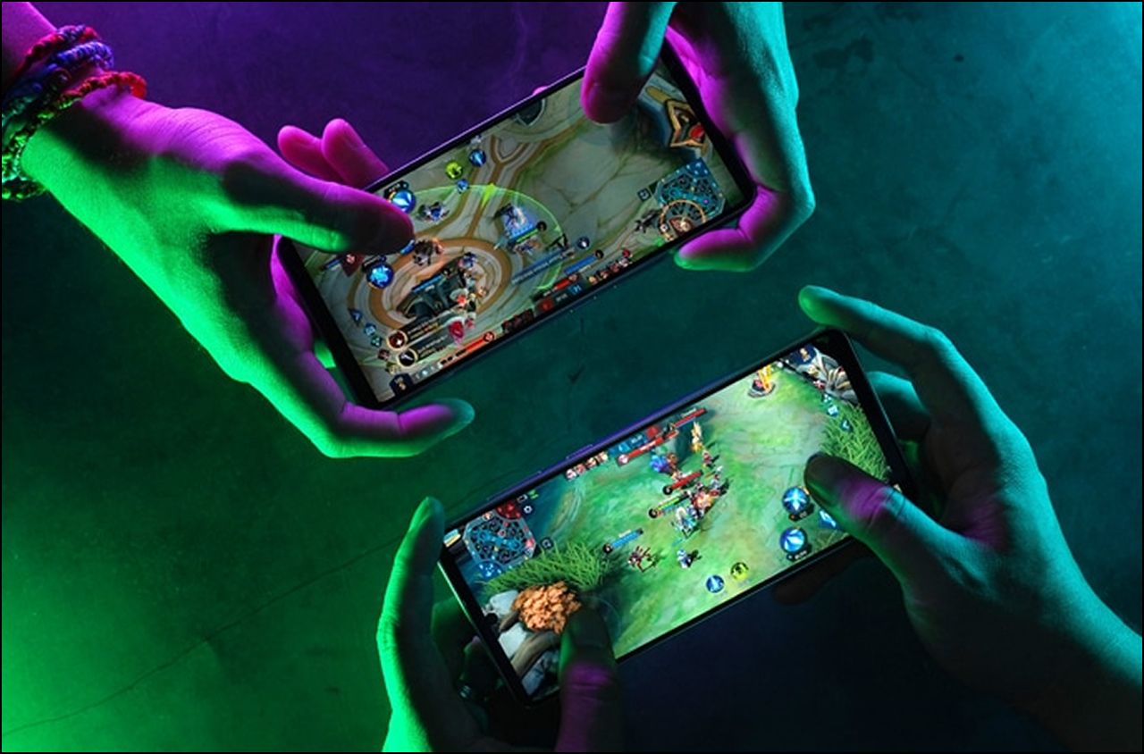 Dua pemain bermain permainan mudah alih pada telefon pintar di bawah cahaya neon hijau dan ungu